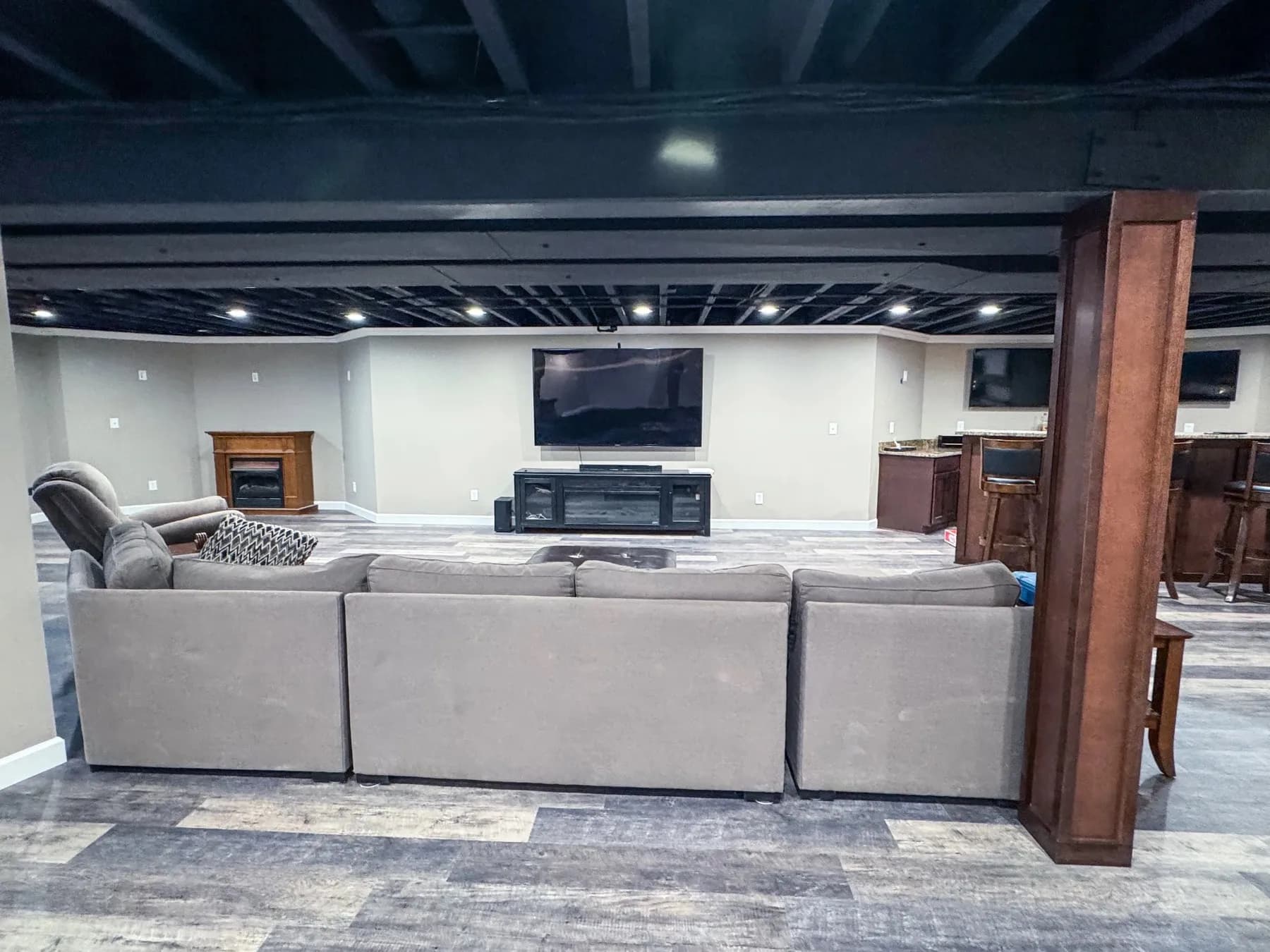 Finished basement family room with a sectional, mounted television, and stained wood support columns