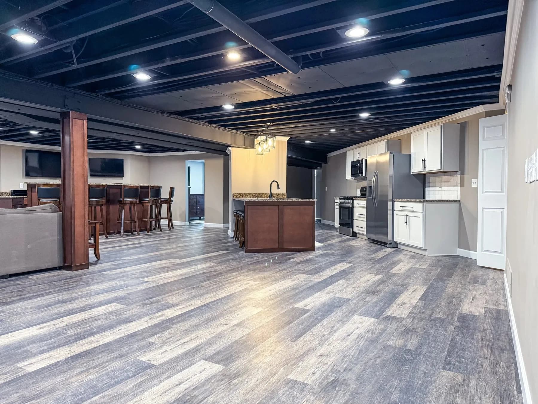 Finished basement with a wet bar, wood posts, and an open black-painted ceiling