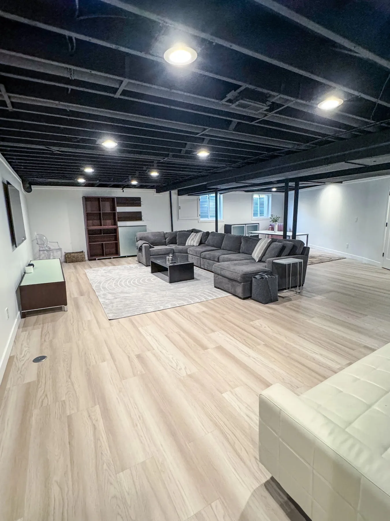Finished basement living area with light flooring and a black painted open ceiling