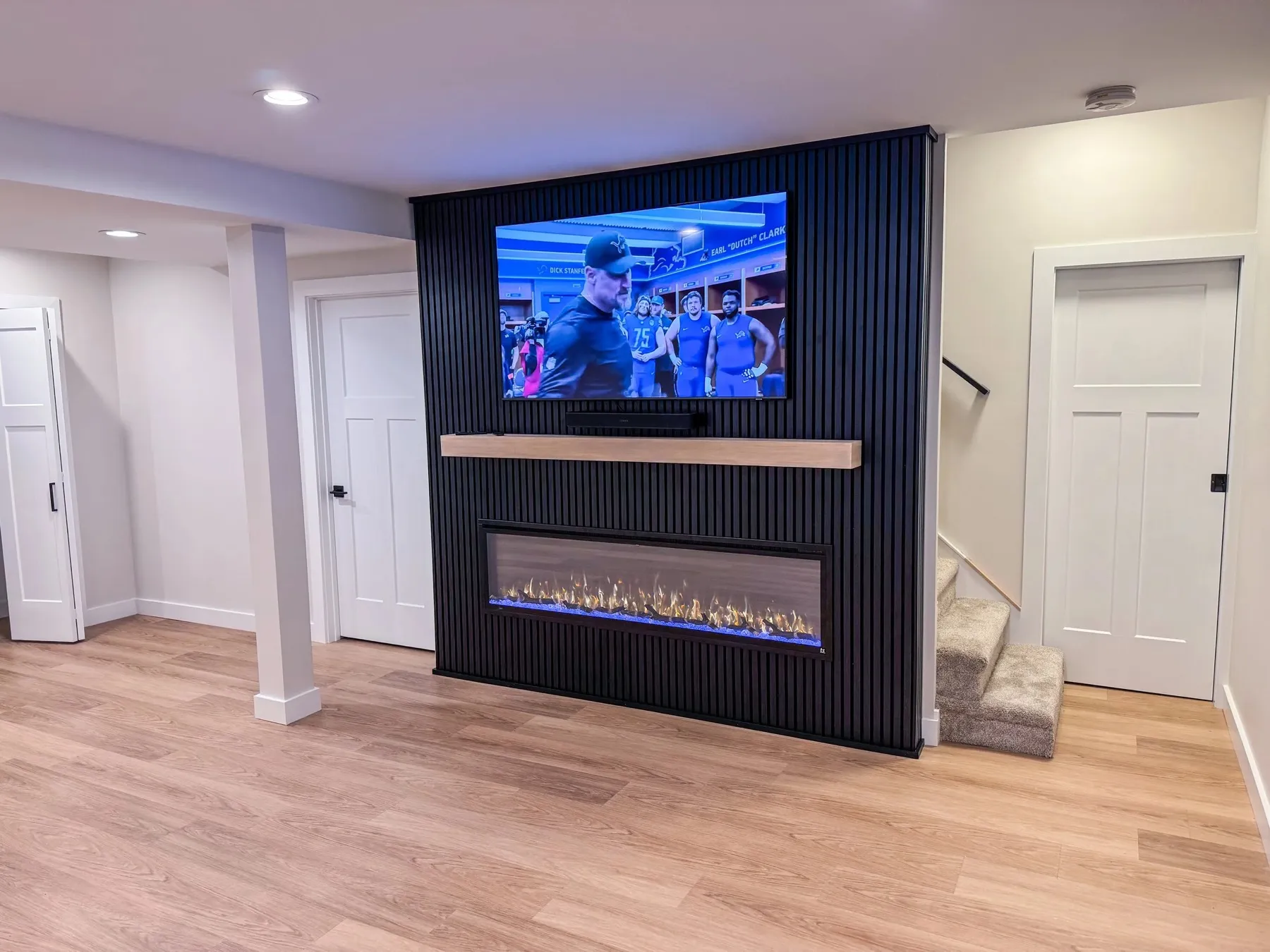 Basement living space with a linear electric fireplace set into a black slat wall below a television