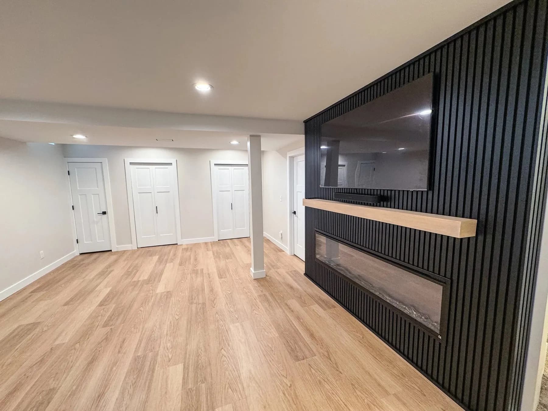 Open finished basement with a black slat accent wall, fireplace, and light wood-look floor