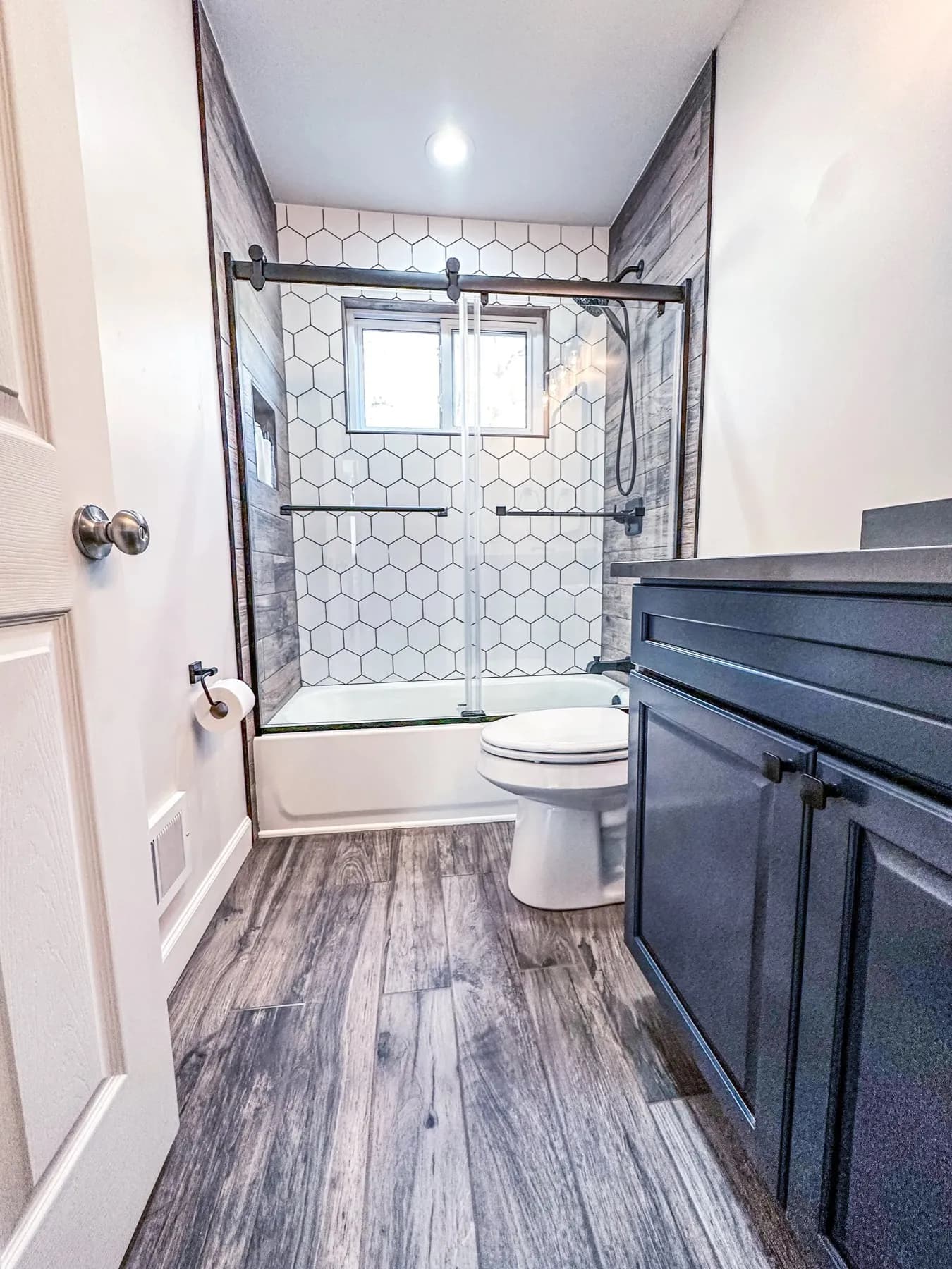 Bathroom with a tiled tub surround, dark wood vanity, and wood-look tile floor
