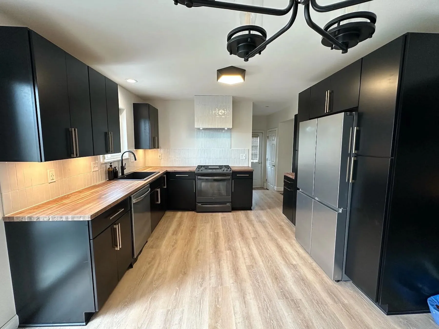 Kitchen with dark navy cabinets, butcher block counters, and light wood-look flooring