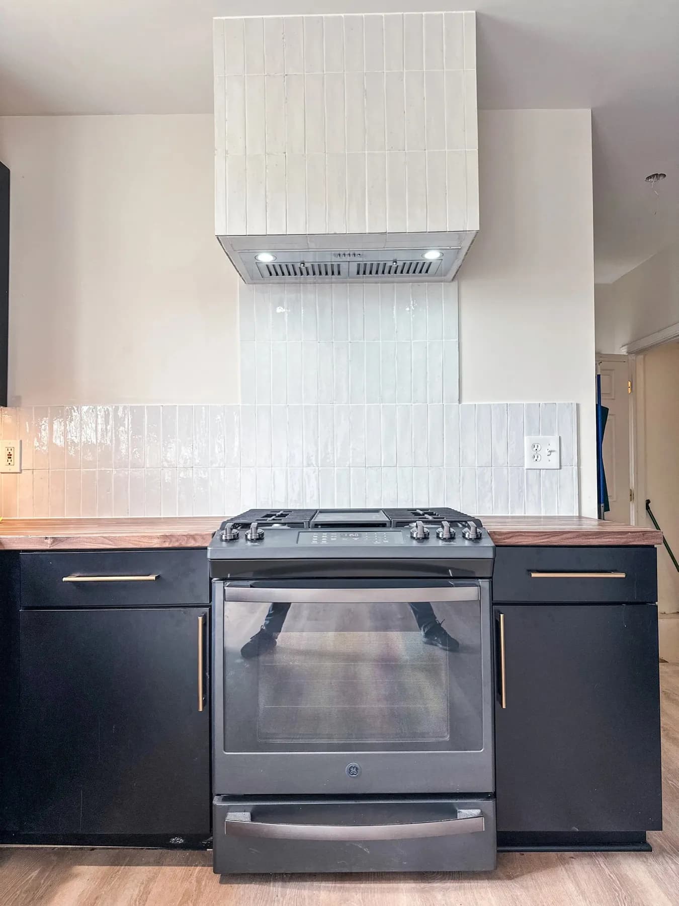Kitchen with black cabinets, a white vent hood, butcher block counter, and a slide-in range